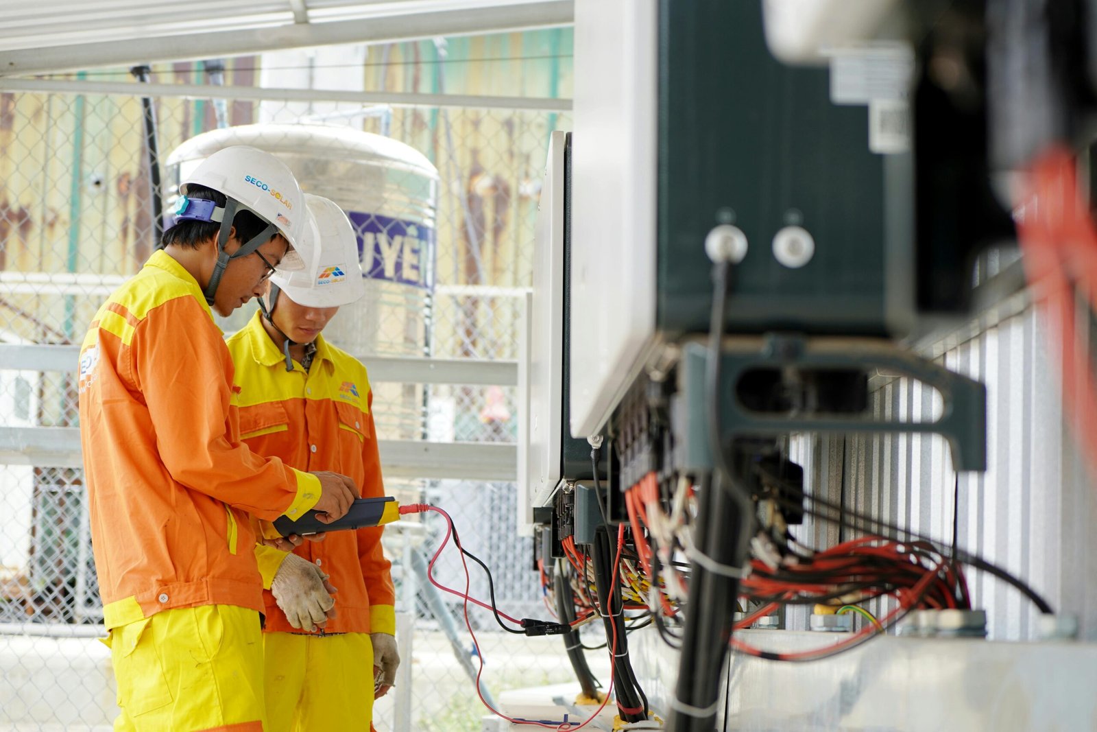 Two technicians with helmets working on electrical equipment outdoors, ensuring safety.