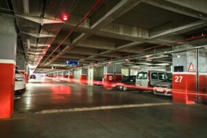Long exposure of an underground parking garage with vehicles and vibrant red light trails.